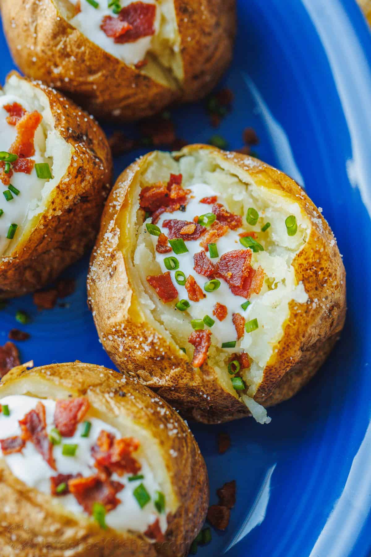 Baked potatoes on a blue plate, topped with sour cream, bacon, and chives.