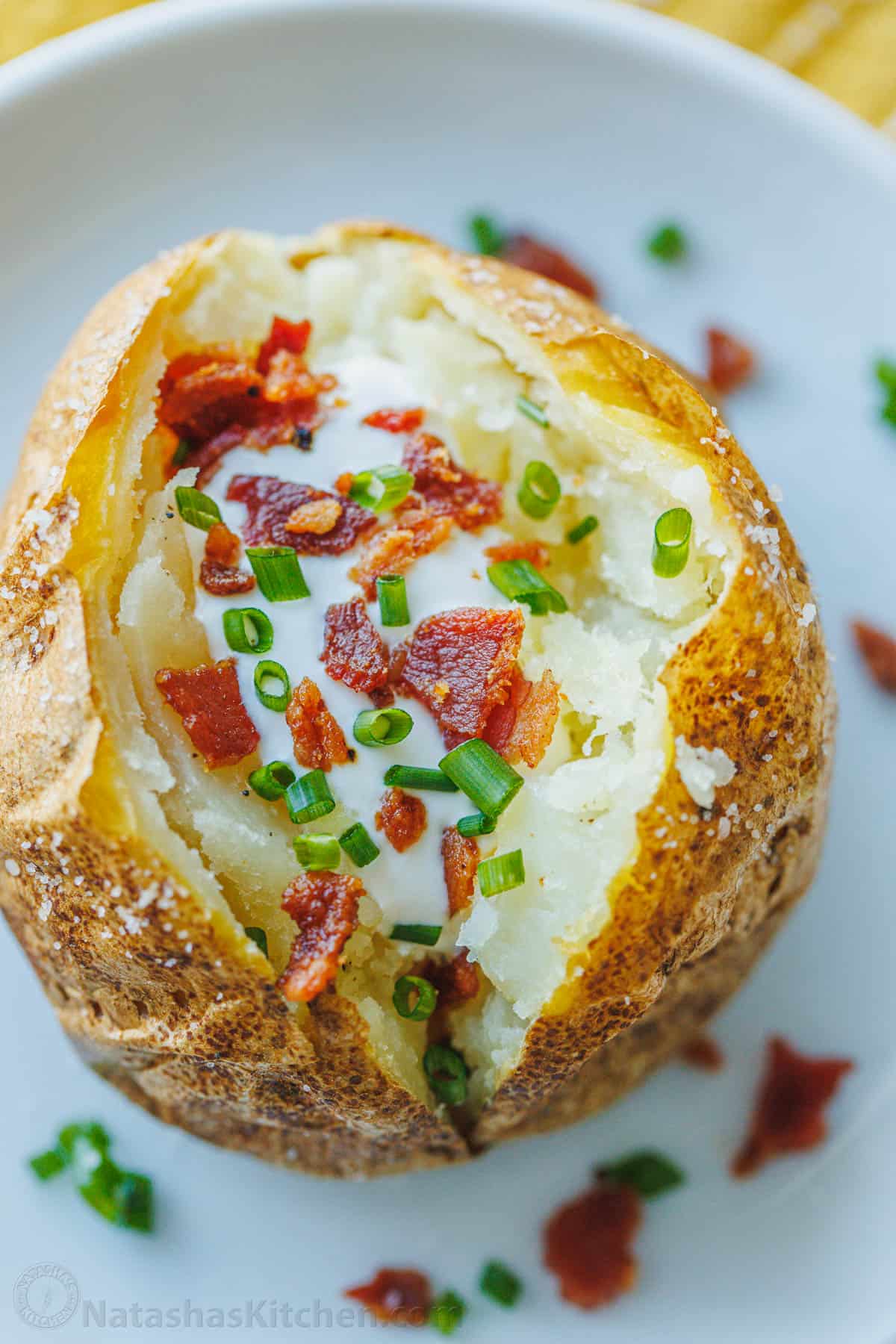 A perfect baked potato on a plate topped with sour cream, bacon, and chives.
