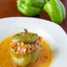 A plate of beef stuffed bell peppers with two raw green peppers behind the plate