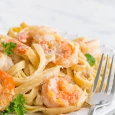 Creamy shrimp alfredo pasta on a plate with a fork beside it