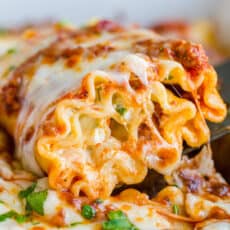 Lasagna roll being scooped out of casserole dish with cheese pull